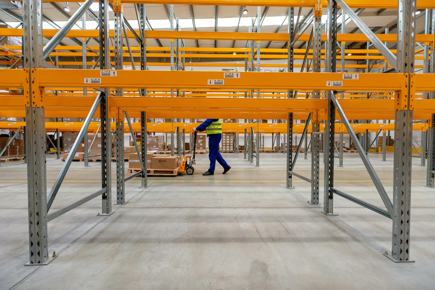 Worker pulling a pallet of boxes through warehouse racking